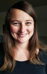 Zu sehen ist ein Portrait von Sarah Rügemer, einer Frau mit in Schwarz vor schwarzem Hintergrund, Ihre Ansprechpartnerin in der Verwaltung der vhs Weilheim